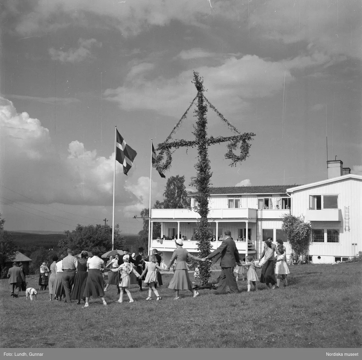 Motiv: Lerdalshöjden ;
Porträtt av en flicka som håller blommor, vuxna och barn dansar runt en midsommarstång, tre män i folkdräkt spelar fiol vid en midsommarstång.