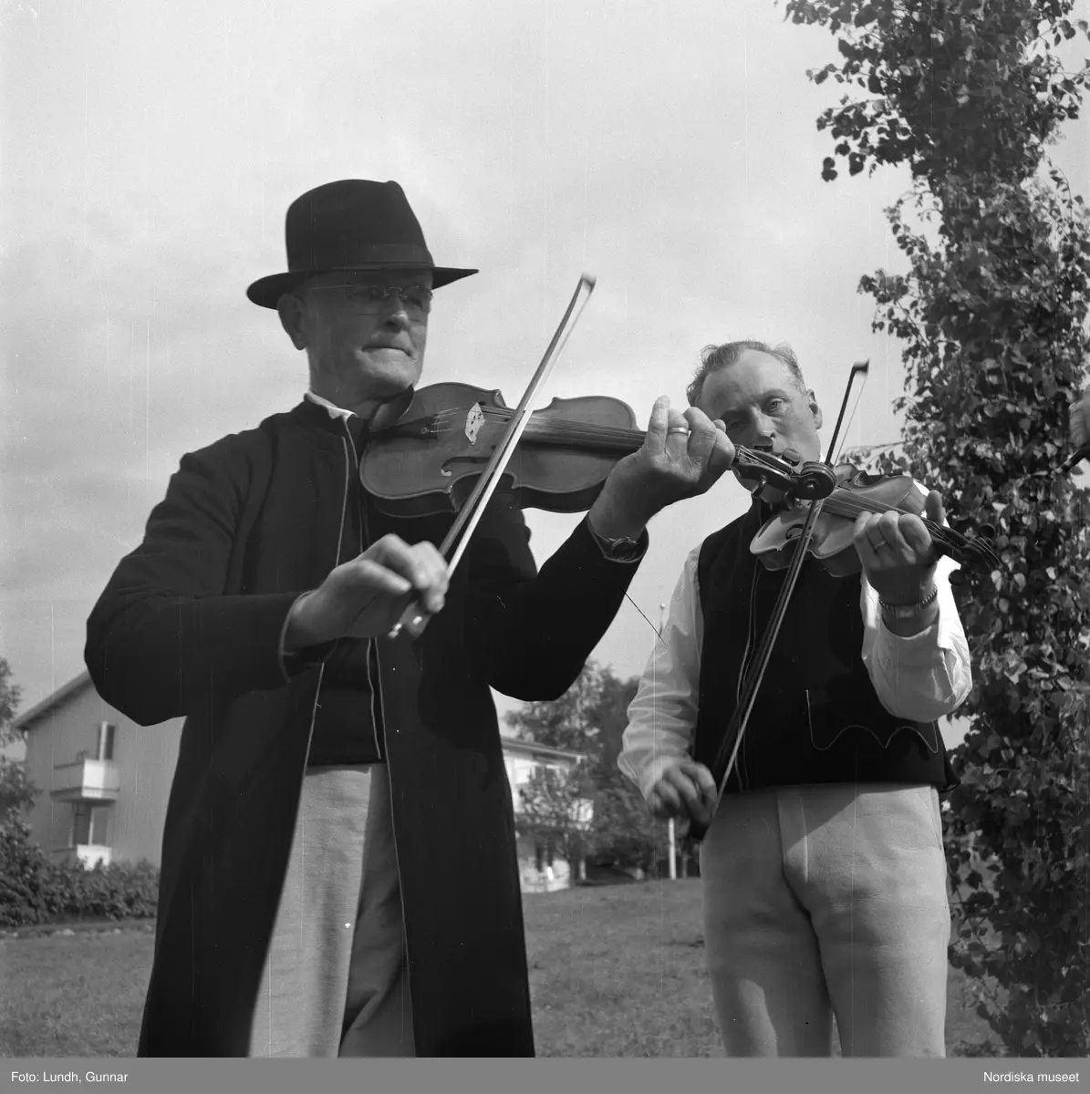 Motiv: Lerdalshöjden ;
Porträtt av en flicka som håller blommor, vuxna och barn dansar runt en midsommarstång, tre män i folkdräkt spelar fiol vid en midsommarstång.