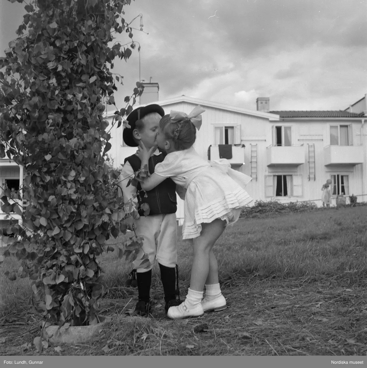 Motiv: midsommarfirande i Rättvik - Leksand ;
En pojke i folkdräkt och en flicka står vid en midsommarstång, en flicka pussar en pojke, en kvinna och en man handlar trasmattor av en man i en försäljningsvagn med text "Hemslöjd", en kvinna står vid en bil med kopparsaker till försäljning och en skylt "Ruben I Redin", en kvinna och en man i folkdräkt håller lövade ringar, kvinnor i folkdräkt går på en väg, en man kör en hästdragen vagn, ett led av kvinnor och män i folkdräkt bär en lövad girlang, människor åker på hästdragna vagnar.