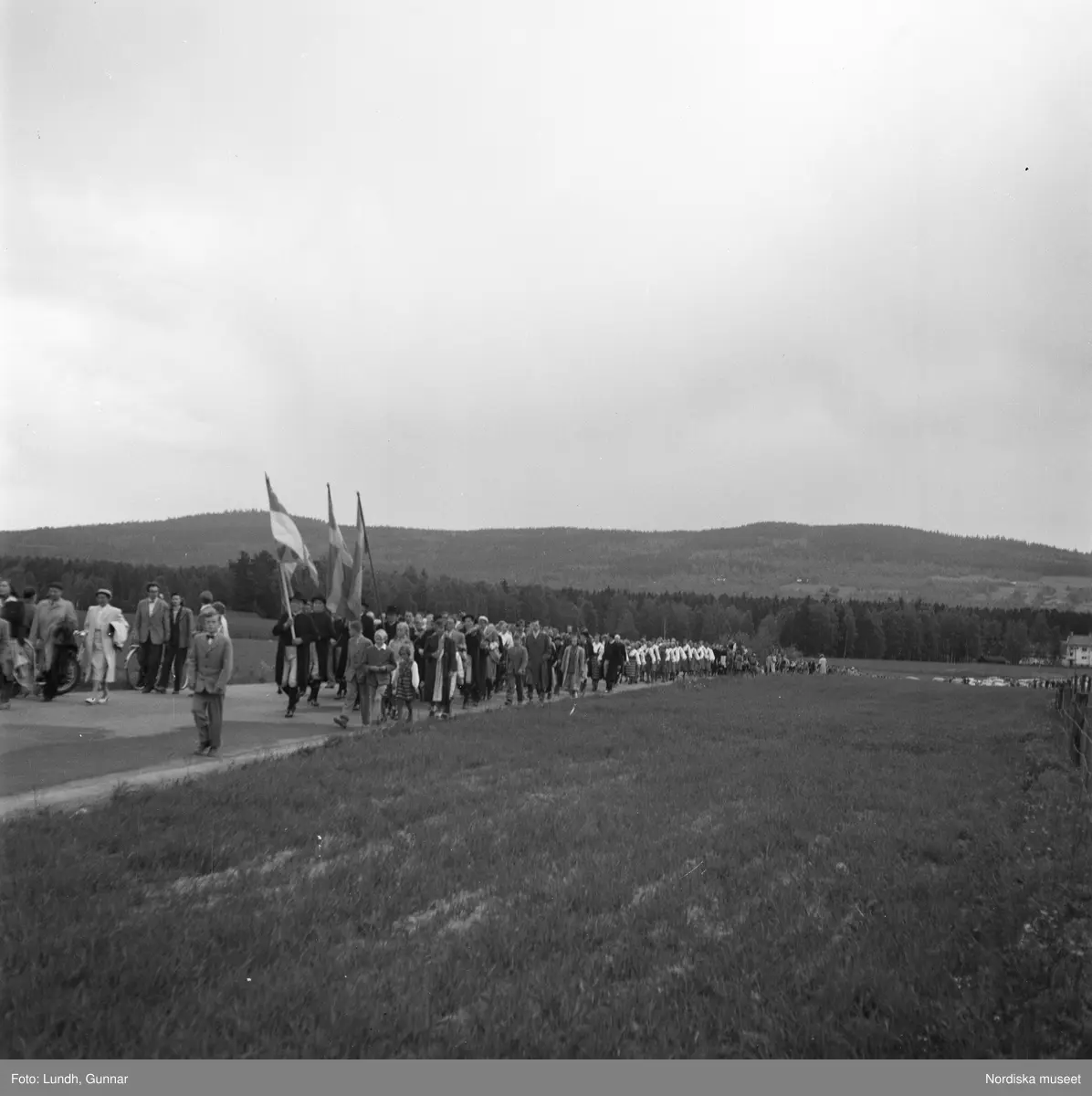 Motiv: (ingen anteckning) ;
Porträtt av en kvinna i folkdräkt och en man som sitter på marken, män och kvinnor i folkdräkt går i ett proccesionståg med flaggor och kvinnor bär en lövad girlang, människor åker på en hästdragen vagn, en folksamling går i ett processionståg.