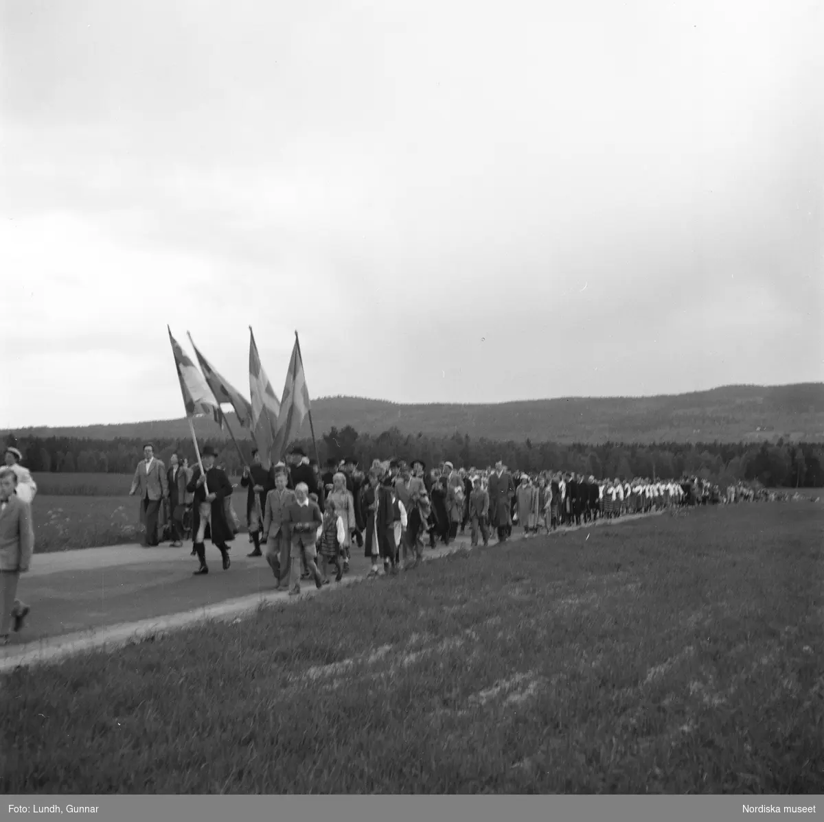 Motiv: (ingen anteckning) ;
Porträtt av en kvinna i folkdräkt och en man som sitter på marken, män och kvinnor i folkdräkt går i ett proccesionståg med flaggor och kvinnor bär en lövad girlang, människor åker på en hästdragen vagn, en folksamling går i ett processionståg.