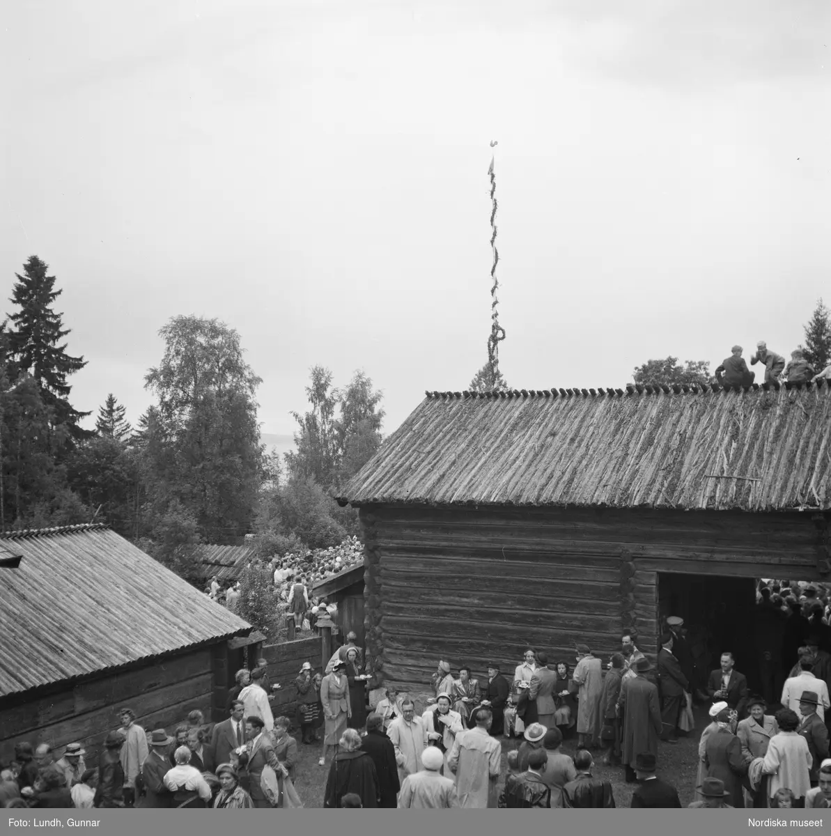 Motiv: (ingen anteckning) ;
En folksamling står kring en midsommarstång, en folksamling vid ett hus, en kyrkbåt ros av kvinnor och män i folkdräkt, en folksamling står vid en brygga med en kyrkbåt.