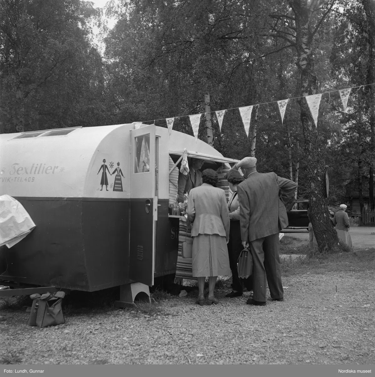 Motiv: midsommarfirande i Rättvik - Leksand ;
En pojke i folkdräkt och en flicka står vid en midsommarstång, en flicka pussar en pojke, en kvinna och en man handlar trasmattor av en man i en försäljningsvagn med text "Hemslöjd", en kvinna står vid en bil med kopparsaker till försäljning och en skylt "Ruben I Redin", en kvinna och en man i folkdräkt håller lövade ringar, kvinnor i folkdräkt går på en väg, en man kör en hästdragen vagn, ett led av kvinnor och män i folkdräkt bär en lövad girlang, människor åker på hästdragna vagnar.