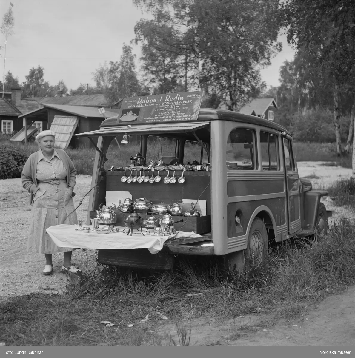 Motiv: midsommarfirande i Rättvik - Leksand ;
En pojke i folkdräkt och en flicka står vid en midsommarstång, en flicka pussar en pojke, en kvinna och en man handlar trasmattor av en man i en försäljningsvagn med text "Hemslöjd", en kvinna står vid en bil med kopparsaker till försäljning och en skylt "Ruben I Redin", en kvinna och en man i folkdräkt håller lövade ringar, kvinnor i folkdräkt går på en väg, en man kör en hästdragen vagn, ett led av kvinnor och män i folkdräkt bär en lövad girlang, människor åker på hästdragna vagnar.