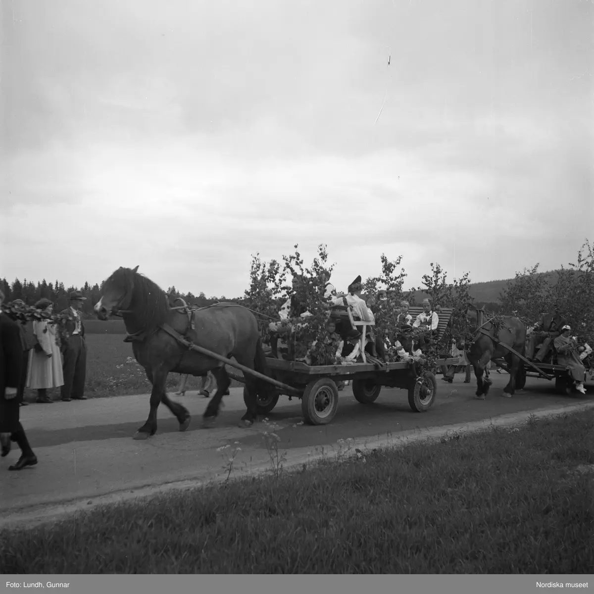 Motiv: (ingen anteckning) ;
Porträtt av en kvinna i folkdräkt och en man som sitter på marken, män och kvinnor i folkdräkt går i ett proccesionståg med flaggor och kvinnor bär en lövad girlang, människor åker på en hästdragen vagn, en folksamling går i ett processionståg.