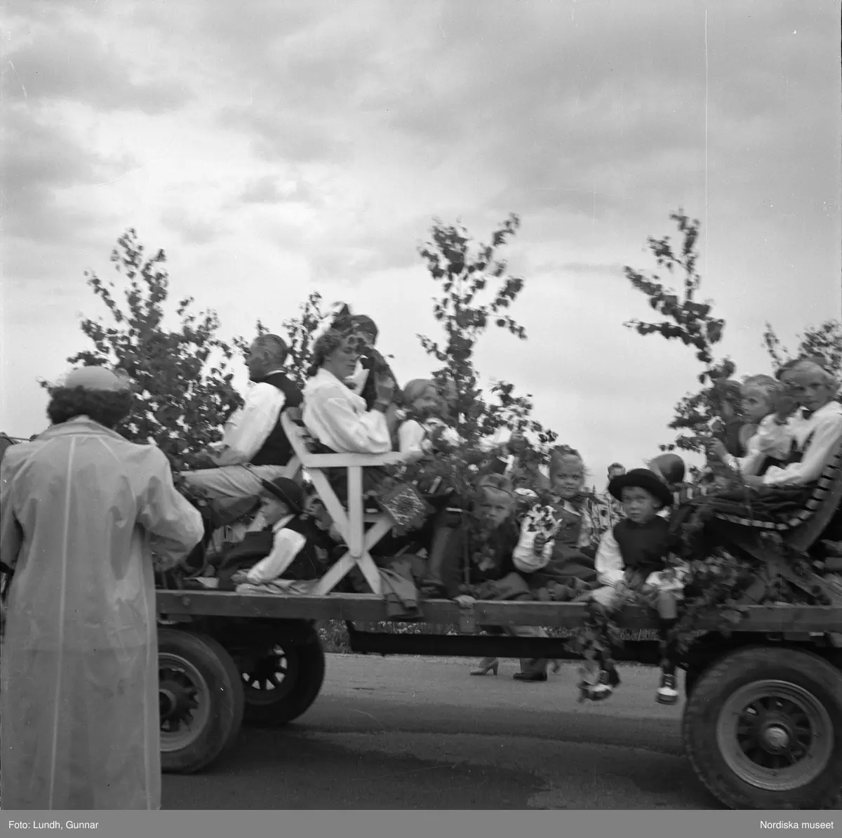 Motiv: (ingen anteckning) ;
Porträtt av en kvinna i folkdräkt och en man som sitter på marken, män och kvinnor i folkdräkt går i ett proccesionståg med flaggor och kvinnor bär en lövad girlang, människor åker på en hästdragen vagn, en folksamling går i ett processionståg.