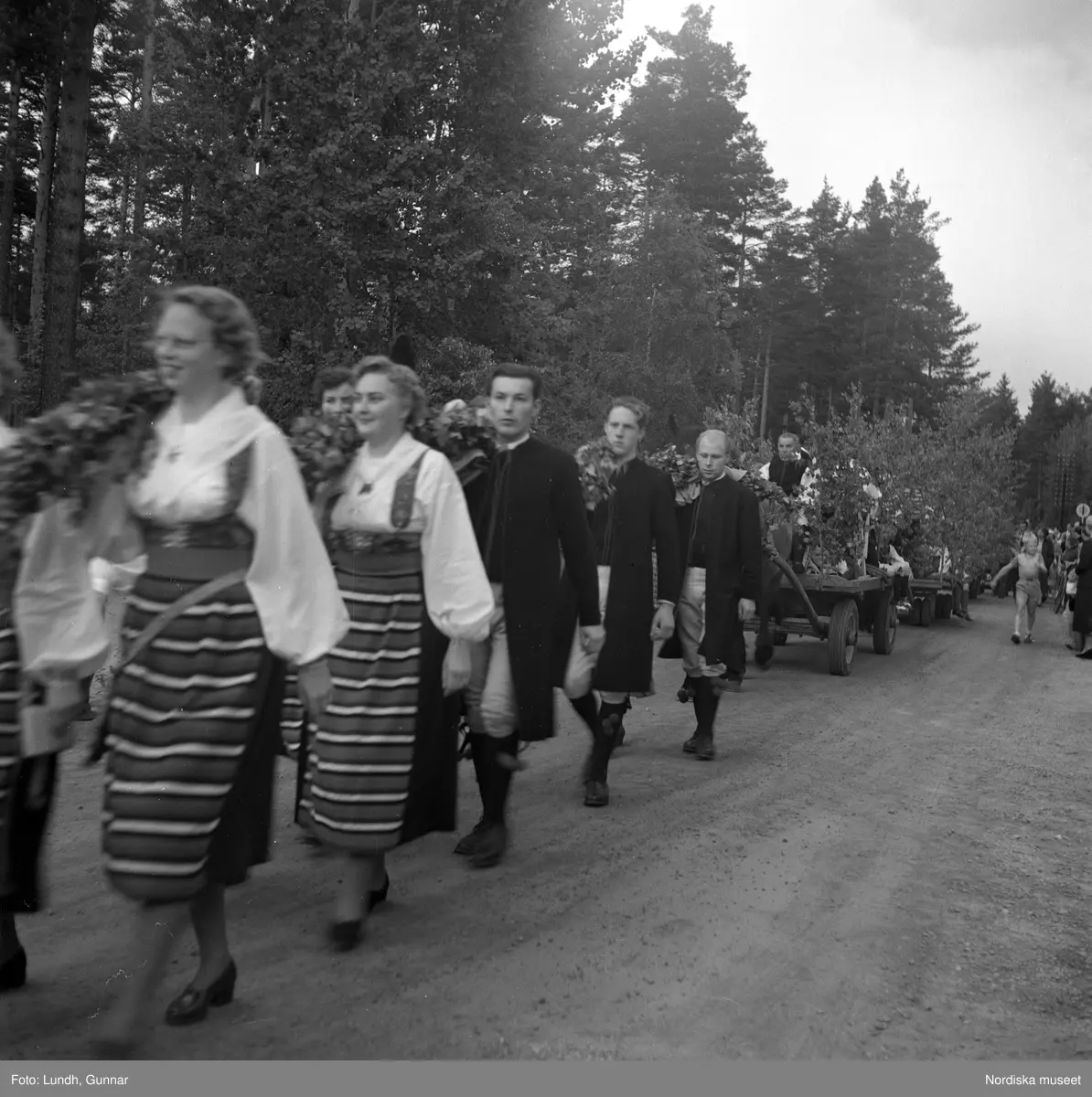 Motiv: midsommarfirande i Rättvik - Leksand ;
En pojke i folkdräkt och en flicka står vid en midsommarstång, en flicka pussar en pojke, en kvinna och en man handlar trasmattor av en man i en försäljningsvagn med text "Hemslöjd", en kvinna står vid en bil med kopparsaker till försäljning och en skylt "Ruben I Redin", en kvinna och en man i folkdräkt håller lövade ringar, kvinnor i folkdräkt går på en väg, en man kör en hästdragen vagn, ett led av kvinnor och män i folkdräkt bär en lövad girlang, människor åker på hästdragna vagnar.