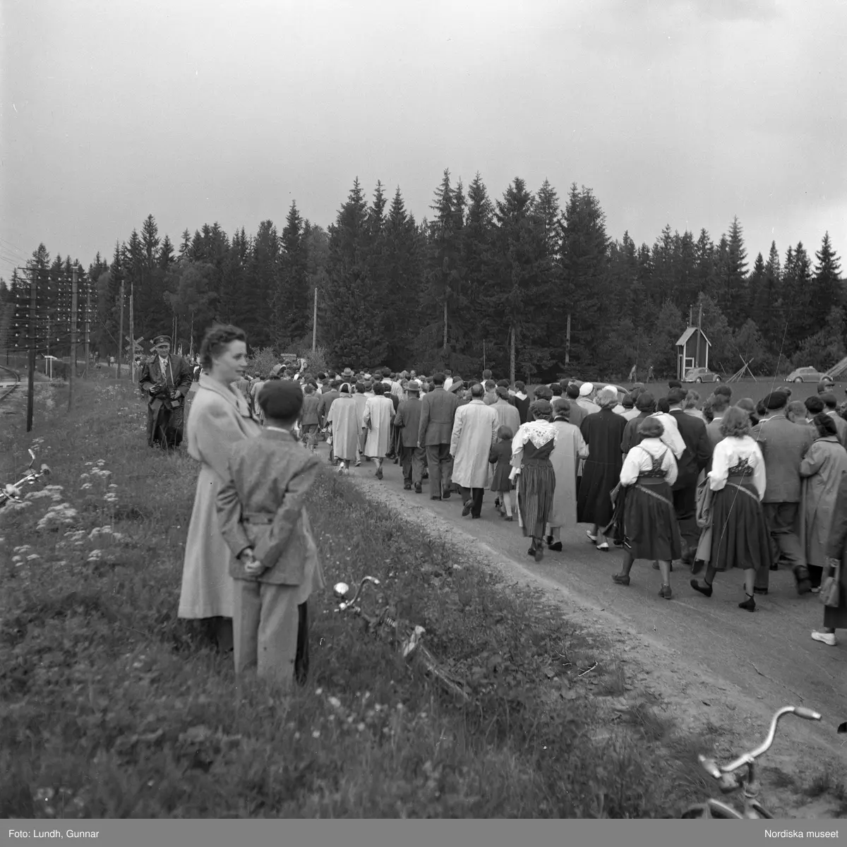 Motiv: (ingen anteckning) ;
Porträtt av en kvinna i folkdräkt och en man som sitter på marken, män och kvinnor i folkdräkt går i ett proccesionståg med flaggor och kvinnor bär en lövad girlang, människor åker på en hästdragen vagn, en folksamling går i ett processionståg.
