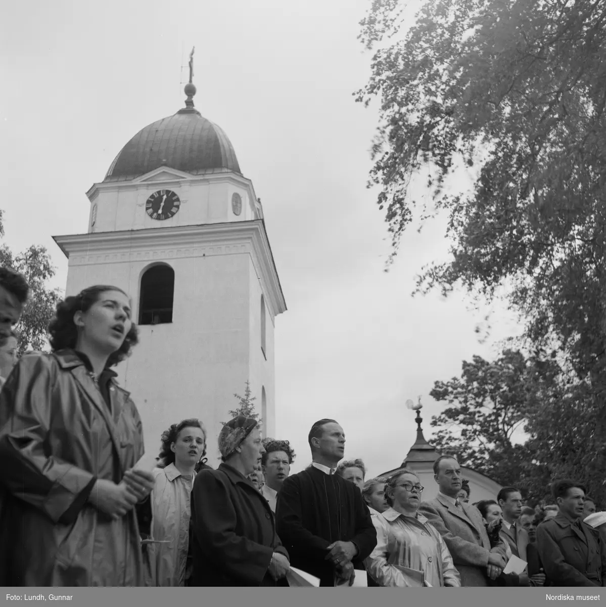 Motiv: (ingen anteckning) ;
En folksamling vid Rättviks kyrka, en folksamling står vid en brygga när kvinnor och män går ombord på två kyrkbåtar.
