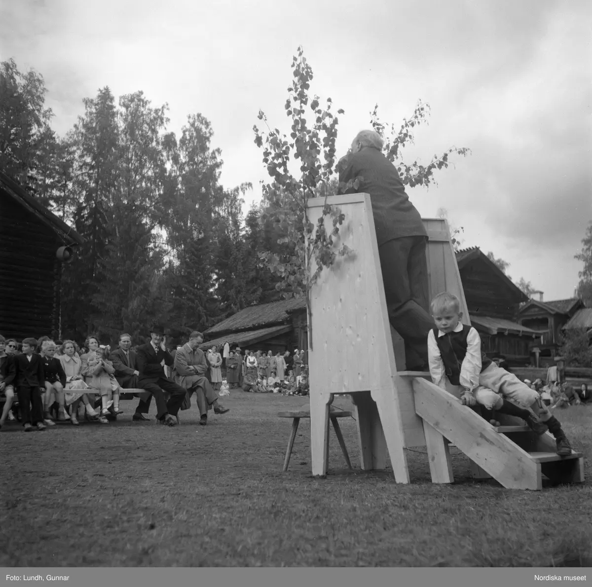 Motiv: (ingen anteckning) ;
Två män i folkdräkt håller fioler, en man i en talarstol talar till en folksamling, ett barn sitter på trapan till en talarstol, en folksamling vid en midsommarstång, porträtt av två varav ett i folkdräkt, kvinnor och män i folkdräkt dansar vid en midsommarstång.
