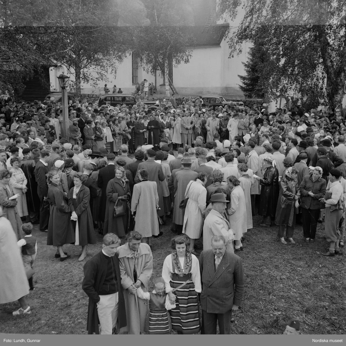 Motiv: (ingen anteckning) ;
En folksamling vid Rättviks kyrka, en folksamling står vid en brygga när kvinnor och män går ombord på två kyrkbåtar.