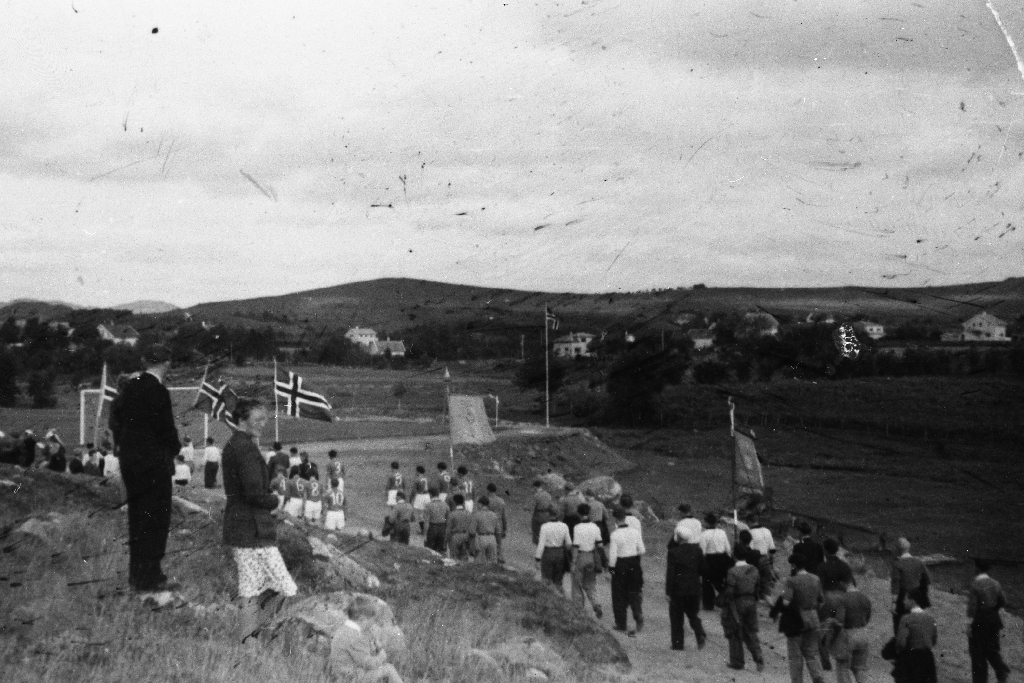 Folk på Frøyland på veg til fotballbanen med Fane og flagg.
Sjå også 1988.5TIM.15.007, 1988.5TIM.15.009 og 1988.5TIM.15.010