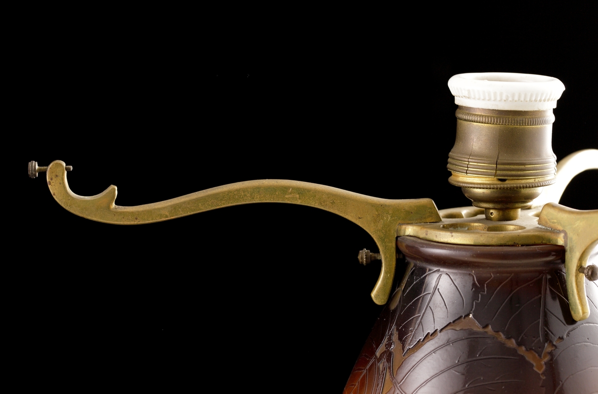 Opak lampa, gul med brunt och grönt växtmotiv i etsat överfång.
Metallfattning för glödlampa. Tvinnad textilsladd.
Etikett: rund: "GALLÉ PARIS NANCY ETABL.TS" Handskrivet i mitten: "23"
Etikett: oval: " ETABL.TS GALLÉ NANCY PARIS"