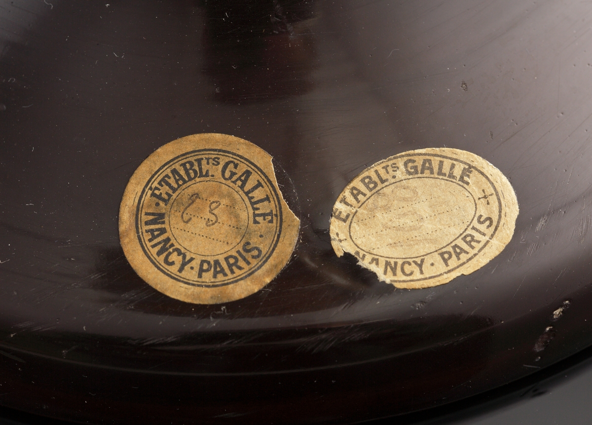 Opak lampa, gul med brunt och grönt växtmotiv i etsat överfång.
Metallfattning för glödlampa. Tvinnad textilsladd.
Etikett: rund: "GALLÉ PARIS NANCY ETABL.TS" Handskrivet i mitten: "23"
Etikett: oval: " ETABL.TS GALLÉ NANCY PARIS"