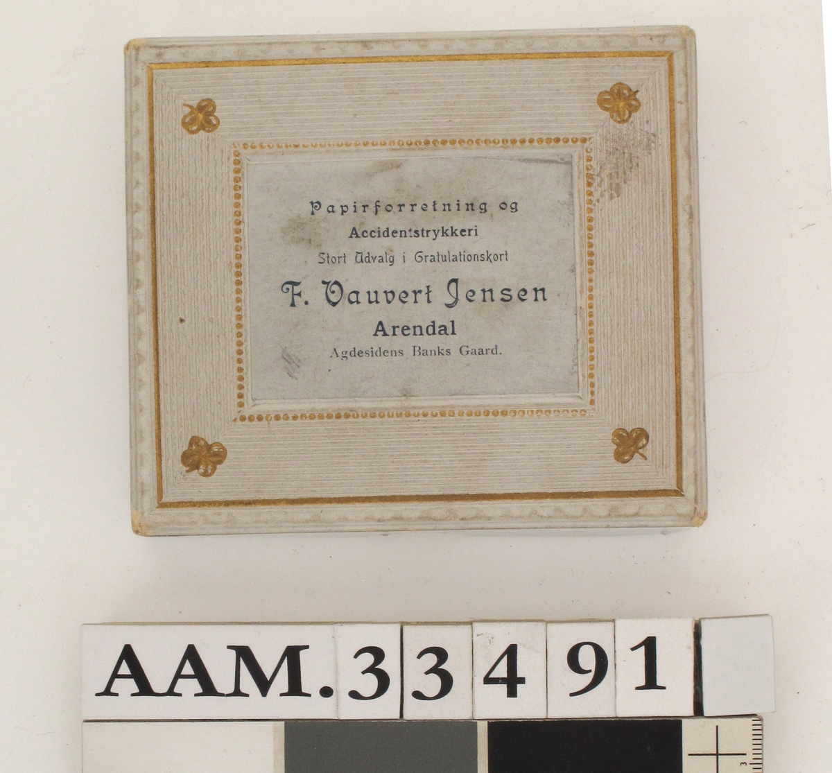 Vareeske av kartong, dekorert med påtrykt mønster og firmanavn. Eskelokket er dekorert med preget mønster, linjer, perler og firkløver.