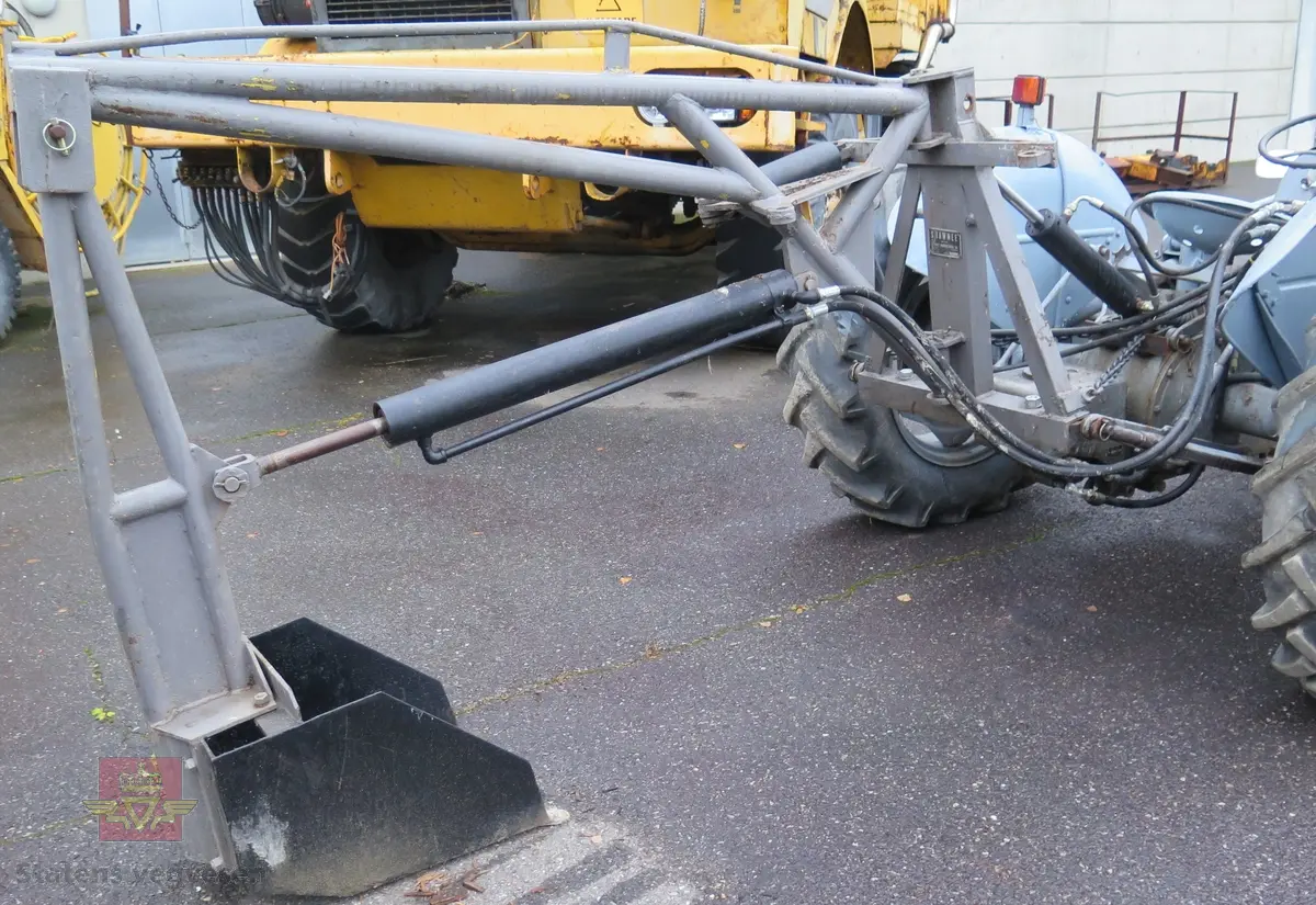 Ferguson TEA20. Grå traktor med lasteapparat foran og graveaggregat bak. Motoren er en 4-sylindret bensinmotor fra Standard Motor Company.