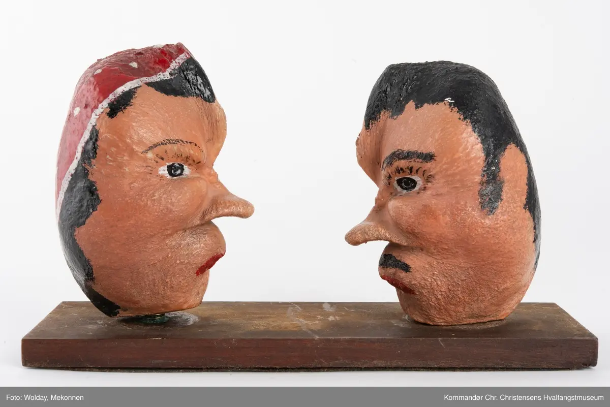 To bemalte øreknokler montert løst på en plate. De er malt som hode til en mann og en dame.