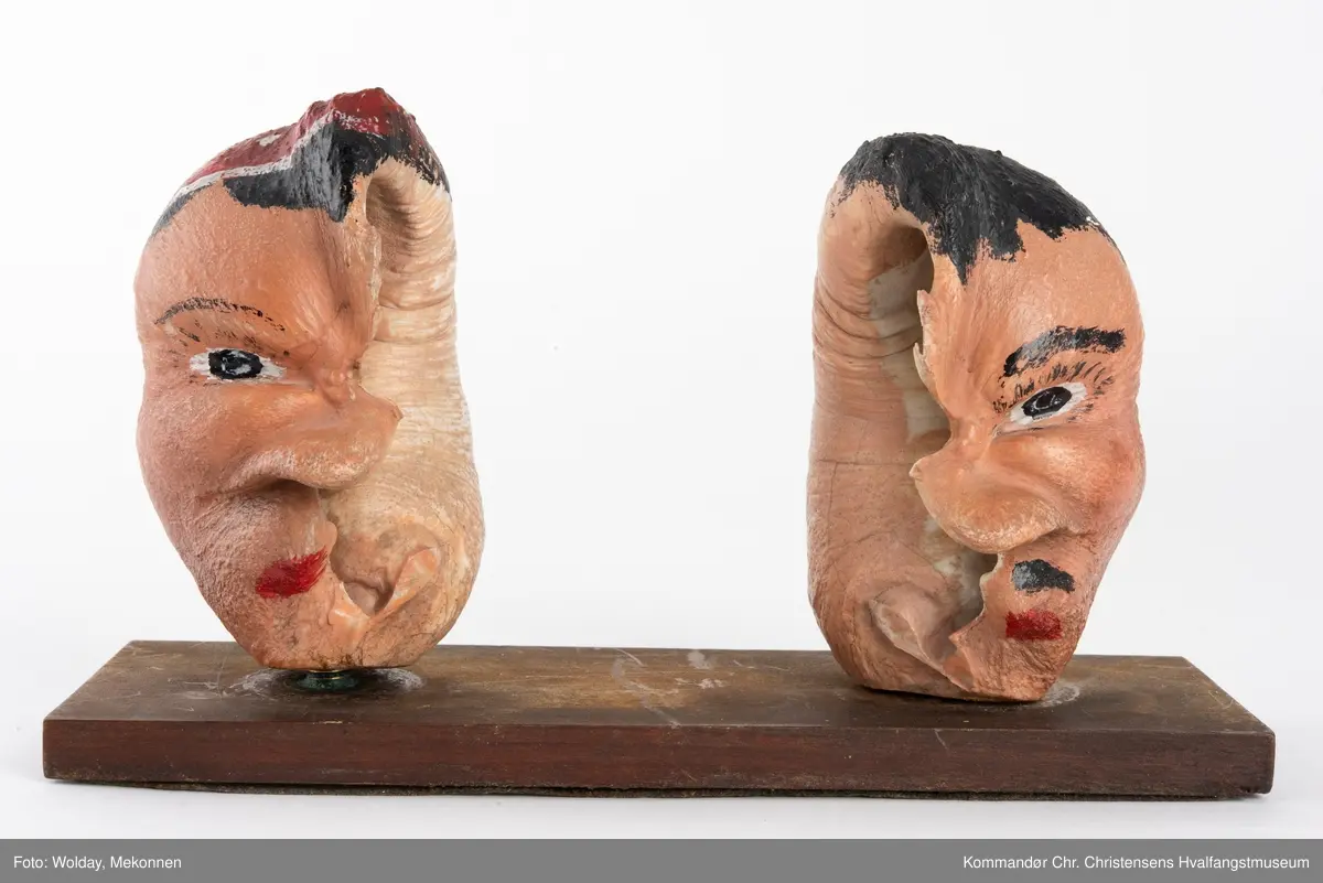 To bemalte øreknokler montert løst på en plate. De er malt som hode til en mann og en dame.