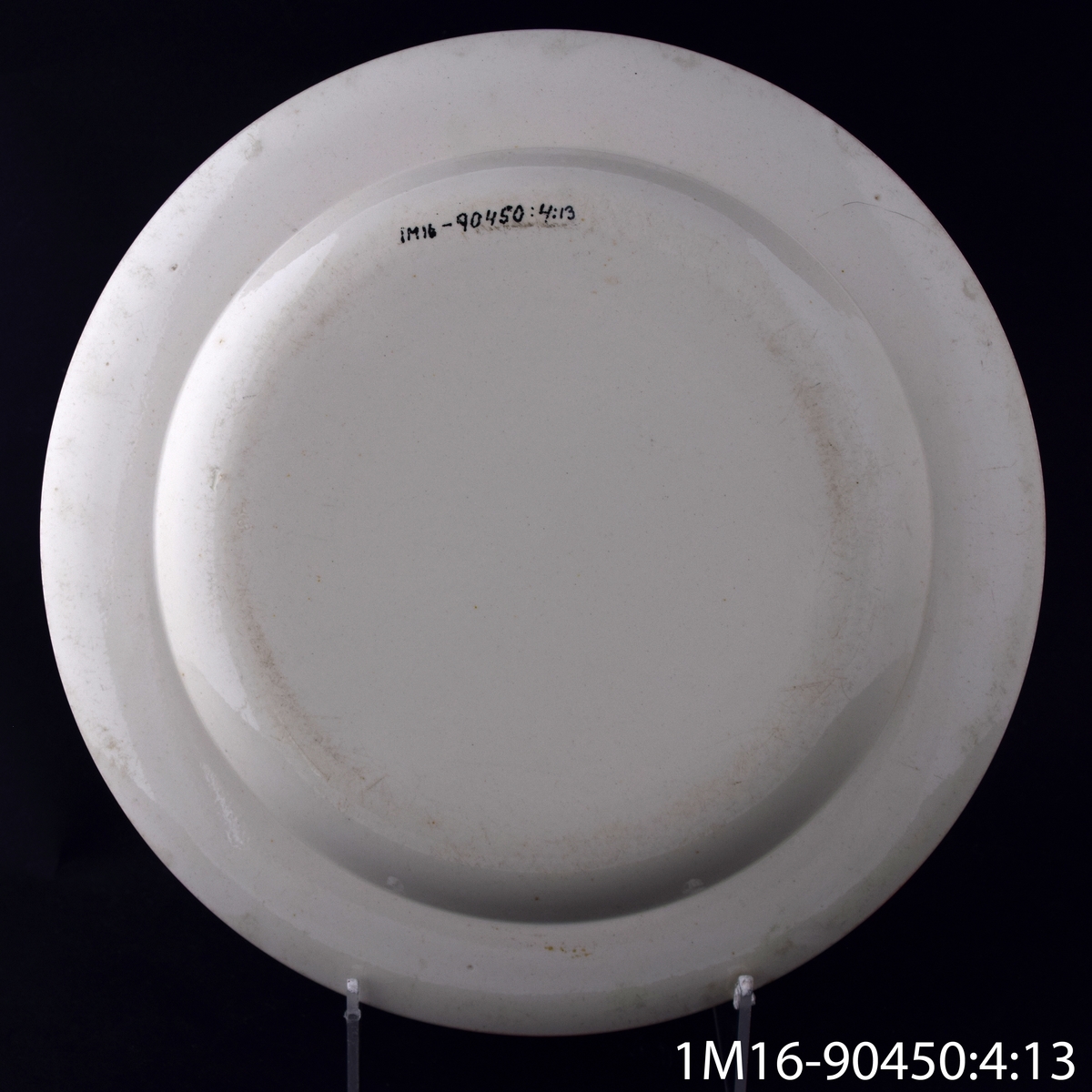 Tallrik, flat, av flintgods, med en bredare och en smalare blå rand längs kanten och initialerna JN, som står för John Nonnen. Tillverkare: Wedgewood.