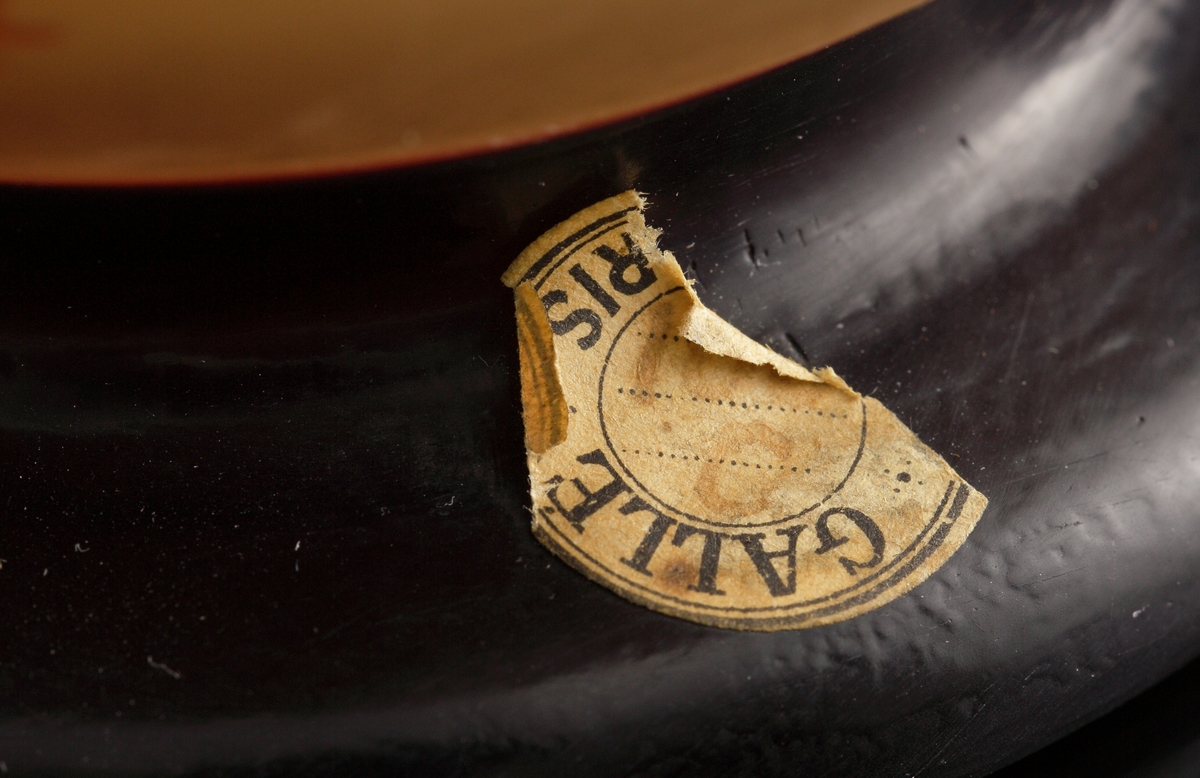 Lampa i skiftande gult, opakt glas. Dekor i rödbrunt etsat överfång. Motivet föreställer nyponkvistar.
Metallfattning för glödlampa. Tvinnad textilsladd.
Etikett: Skadad men "GALLÉ PARIS" kan uttydas.