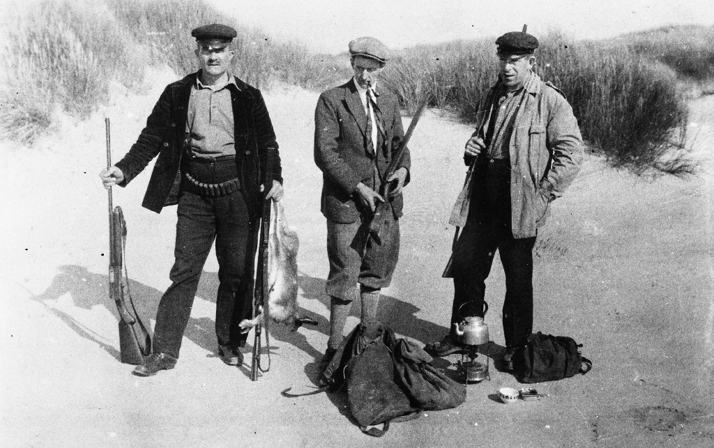 Harejakt i sandkulene på Reve. Til v. mannen med børse og skoten hare er ukjend, Sven Skjæveland sen., og Trygve T. Kverneland.  I sanden "rypesekker" og primus med kaffikjel.