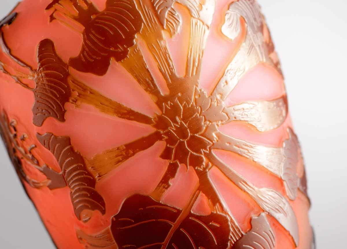 Röd opak vas med blomstermotiv i brunrött etsat överfång.