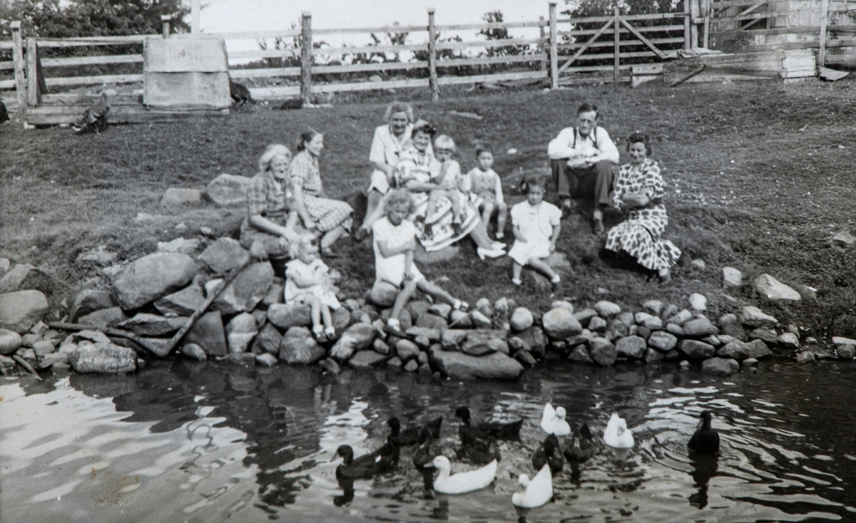 Gruppe 11 personer sittende ved andedammen på Solberg gård, hos Jon og Astrid Sannes-Hagen, Tangen.
Nederst til venstre i første rekke sitter Ragnhild Sannes-Hagen ( (f.1945) gift Fossum). Bakerst til høyre sitter Jon Sannes-Hagen. Andedam, ender, and.