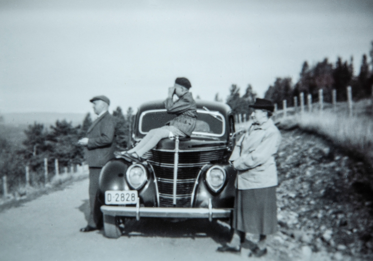 Oskar A. Berg i Opsalbakkene i Vallset, Bilen hans,  D-2828 er en Ford V8 standard 1938-modell. På panseret sitter Jan Arne Berg (da 10 år) å kikker utover. Ved siden av bilen står Oskar`s svigermor, Sigid Olsen.