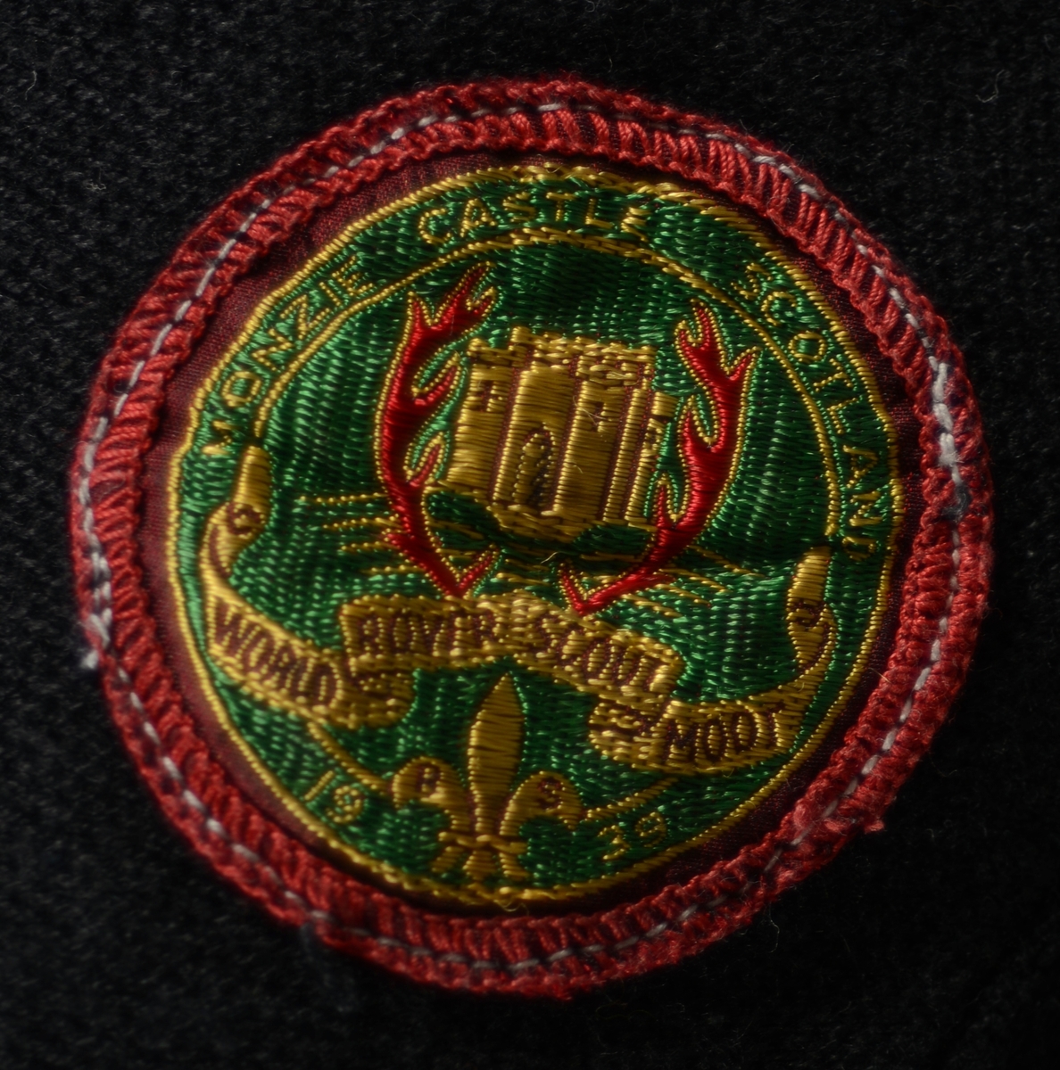 En speiderkappe/leirbålkappe sydd av svart ullstoff som er flossete på innsiden. Kappen har maskinsydde kanter i halsen og nede. Langsidene har jarekanter. Nede på kappen er det påsydde stykker av stoff som gjør at den faller pent nede langs kanten. Kappen har trolig vært fotsid. Halsen er rund når den lukkes. Det er to par med snorer for knyting - et par helt oppe i halsen og et par litt lenger ned på brystet. Det er påsydd flere merker på kappen. De som har tekst er gjengitt under "Påført tekst/merker". Merkene er fra ulike leirer, og de indikerer at det har vært en gutt/mann som har brukt kappen (som "boy scou"t og "rover"). Det er også merker uten tekst som for eksempel det sveitsiske flagget, speiderliljen med og uten rød trekant og en mann/gutt som utøver sport. Noen av merkene er fotografert og vises til slutt i bilderekken.