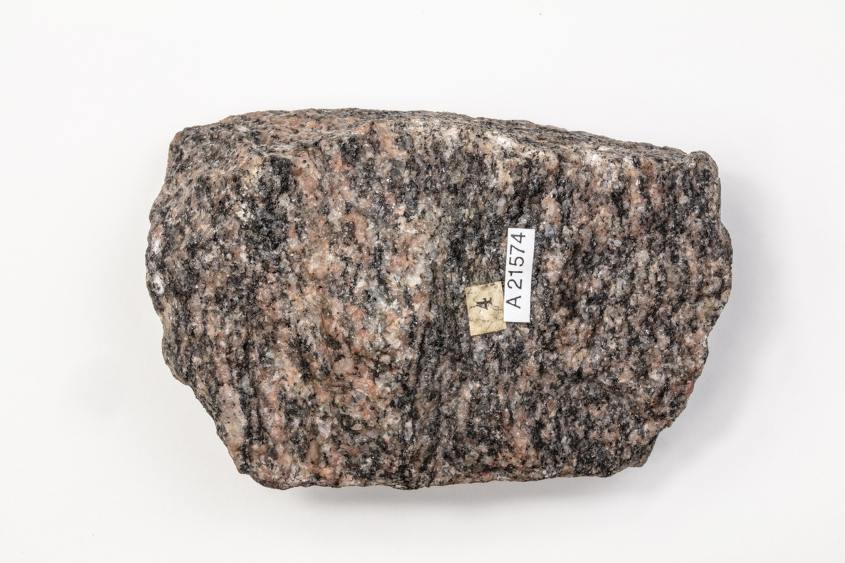 En metamorf bergart. Färgen kan variera beroende på vilka mineral som ingår. Till skillnad från graniten har gnejs en parallellstruktur som gör den lättare att klyvas utefter skiktningen. Exemplaret kommer från Hjälmare kanal, i Söder- och Västmanland och ingår i samlingen från Vänersborgs Allmänna Läroverk.