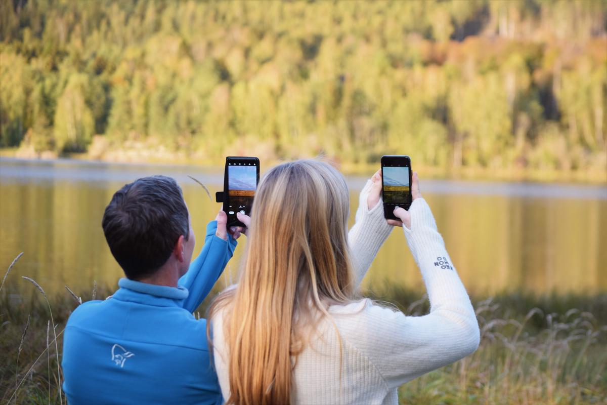 To personer fotograferer i naturen med mobiltelefoner.