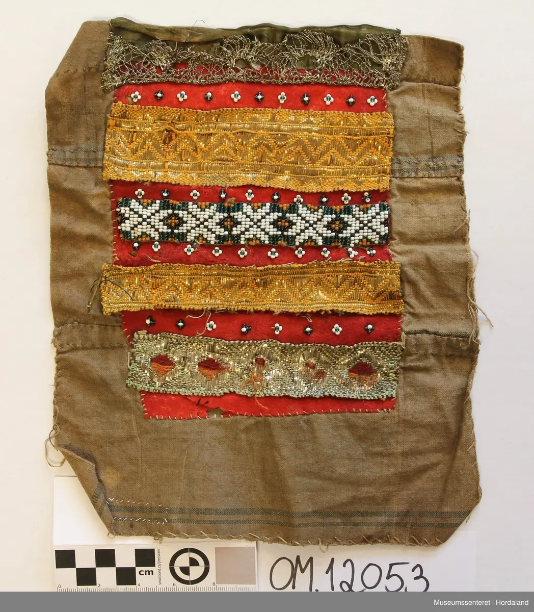 Brungeduk samansett av sylvband og perlebroderi i border. Desse er festa til eit raudt bakstykke av ull. Bakpå der att er det eit større stykke av bomullslerret, sydd saman av 3 remser , har truleg vore kvitt, men er brunt no, med 2 smale blåe striper nedst.
Oppe på framsida har bringeduken fyrst eit grønt silkeband, 2,5 cm breidt. Utanpå der ligg ein sylvknipling. Rett under den er det sydd på nokre småe perlemedaljongar. Så kjem eit breidt (4 cm) forgylt band, ei rad med perlevev, 3 cm, ny rad med forgylt band, 2,5 cm breidt, så dei same perlemedaljongane att, nederst er eit sylvband som det har vore brodert litt på.