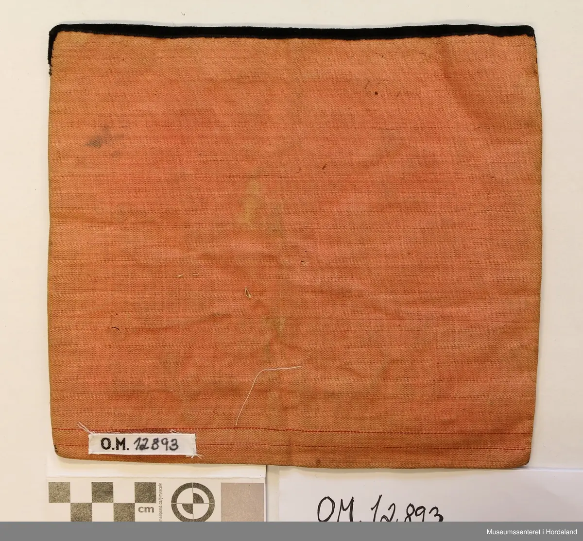 Kvadratisk brystduk i perlebroderi sydd på stramei og broderi innimellom - halve kross-sting. Svart fløyelsband øvst. Brystduk og kanting av eit rosa stoff. Perlebroderiet er sydd av gullfarga og blåe stråperler og kvite småperler og gullfarga store perler i eit åtteblad rosemønster. Mellomromma er fyllt ut av eit broderi (halve kross-sting) i rosa ulltråd.