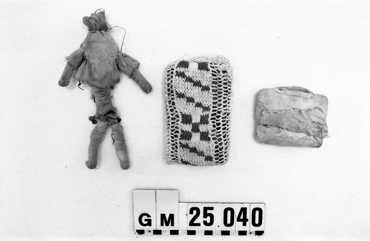 Dyna, till docka.
Stickad remsa med röda rutor. Hopsydd med flätsöm. Fylld innerdyna.
Mönsterstickad med vitt och rött bomullsgarn. Blåvitt bomullstyg och fyllning.