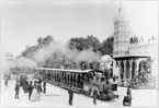 Decauvillejärnvägen under Världsutställningen i Paris 1889, passagerartåg bestående av öppna sommarvagnar samt ånglok vid den tillfälliga stationen (tältet till vänster i bild). Till höger syns Pavillon de lAlgérie.