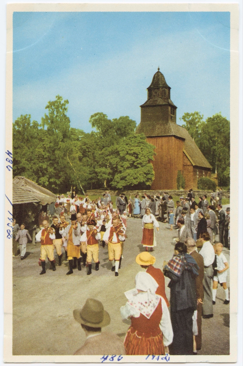 Vykort med motiv från Skansen. "Spelmän och ringleksbarn på Marknadsgatan." I bakgrunden Seglora kyrka.