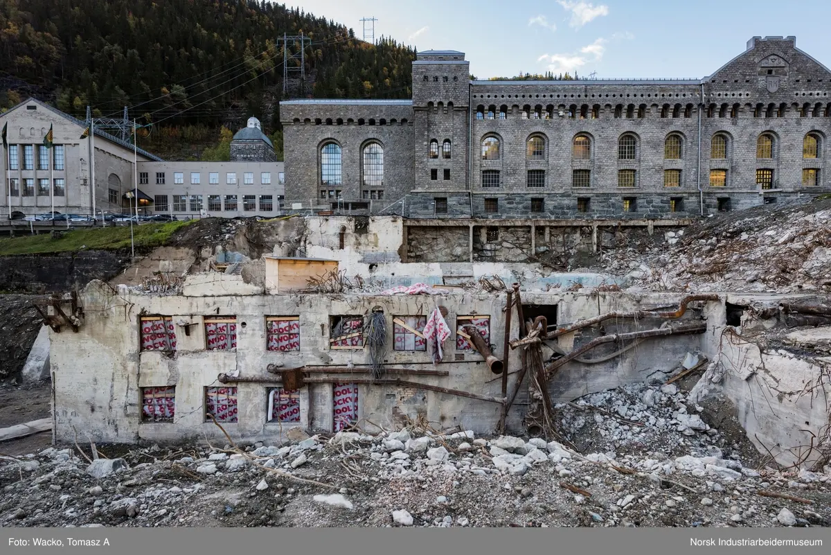 Bygningen var opprinnelig Vemork Hydrogenfabrikk som var plassert fem meter foran Vemork gamle kraftstasjon. Bygget var i betong i 8 etasjer. Driften i bygget stoppet i 1971 og ble i 1977 revet ved sprengning. Telemark Fylkeskommune initierte en utgravning på tomten for om mulig å finne rester etter den gamle kjelleren i 2017. 18.09.2017 startet arbeidet og kjelleren ble i november funnet inntakt.
