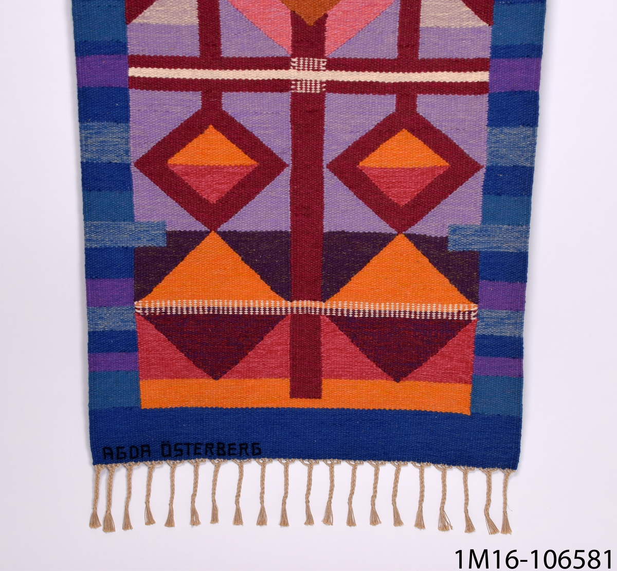 Väggtextil, vävd av Agda Österberg. På övre delen av vävnaden, ett kors.