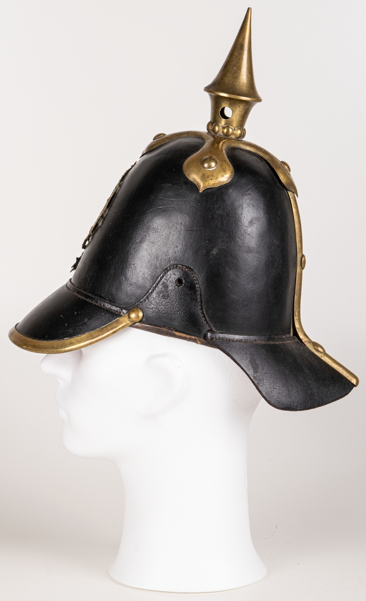 Kask m/1845 för infanteriet. Av pressat svartlackerat läder. hög välvd form med skärm och nackskycdd. Överst mässingspik med korsformat fäste. Skärmen mässingskantad. Framtill emblem i form av lilla riksvapnet i mässing. Hakremmar med fästen saknas. Spännbart "foder" av svart läder. Skrivet på nackskyddets insida. "Otto" samt "23 1/4".
