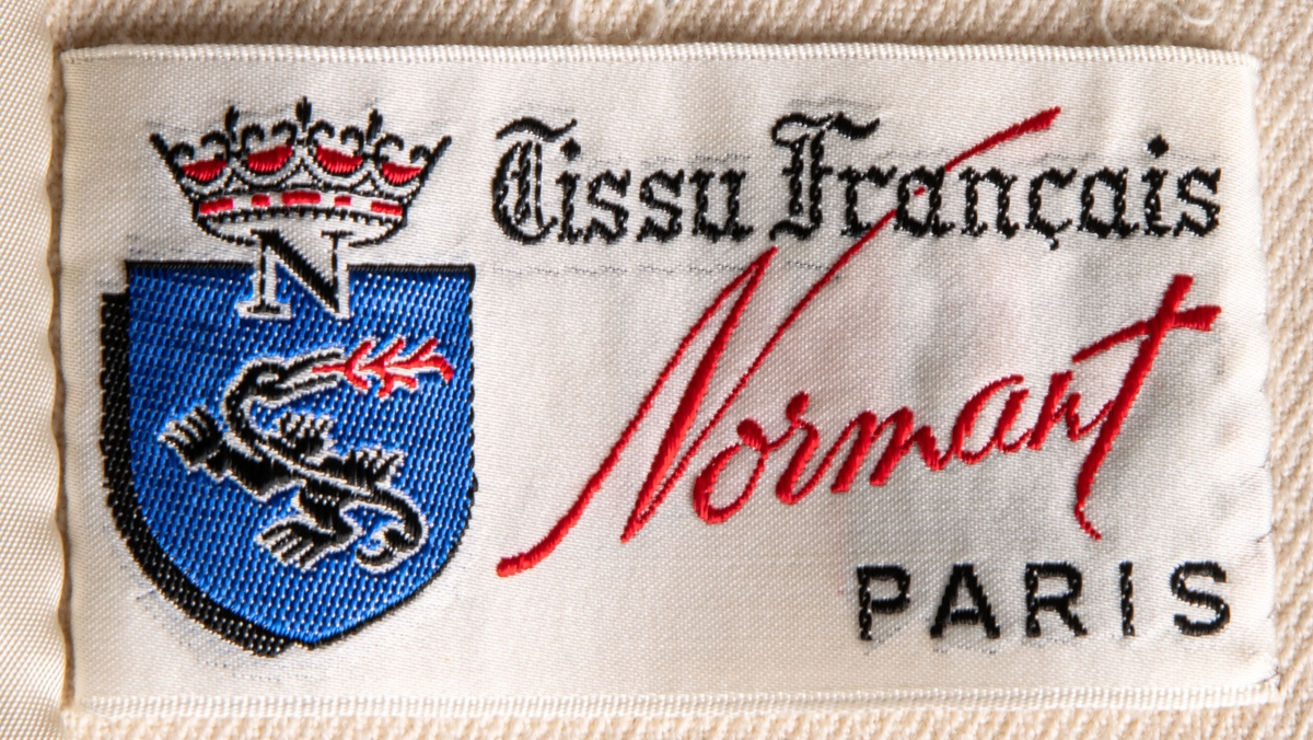 Vit yllekappa av A-modell från 1960-talet. Tillverkad av Tissu Francais Normant, Paris. Stående krage och knäppning med två knappar framtill.