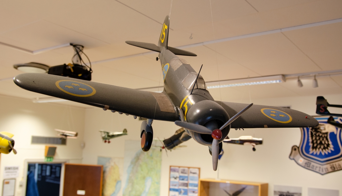 Flygplansmodell av massivt trä i skala 1:20. Modellen är målad enligt Målningsritning för flygplanstypen och märkt med gula siffror 15 samt flottiljbeteckning F 13. Modellen är byggd av Rune Johansson (Termik Johan) Norrköping. B 5 Northrop 8 A1.