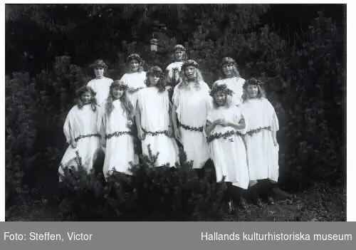 Troligen döttrar till anställda vid Fagereds sanatorium som är uppklädda och utsmyckade för att fira midsommar. (Doktor Steffen hade 9 döttrar så några kan vara hans flickor.) Bild 1: 5 flickor i vita klänningar och tidstypiska pannband med blommor på var sida, håller i blomstersmyckade korgar, alla olika. Bild 2: 10 flickor står i togadräkter i en talldunge med lågt sittande skärp och huvudkransar av blader, kanske lingon.