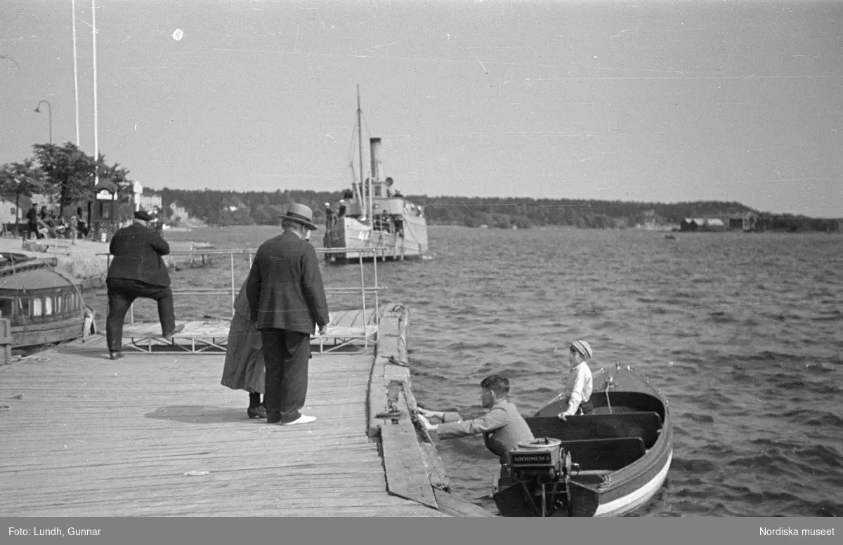 Motiv: Stockholm - Vaxholm;
Människor på en brygga med skylt "Edlunda", en segelbåt, människor på en brygga med skylt "Höganäs".

Motiv: Vaxholm;
Människor står på en brygga och en båt lägger till, en segelbåt, två män lyfter backar med flaskor på en brygga, folksamling vid möbler utställda på en grusplan (troligen en auktion).