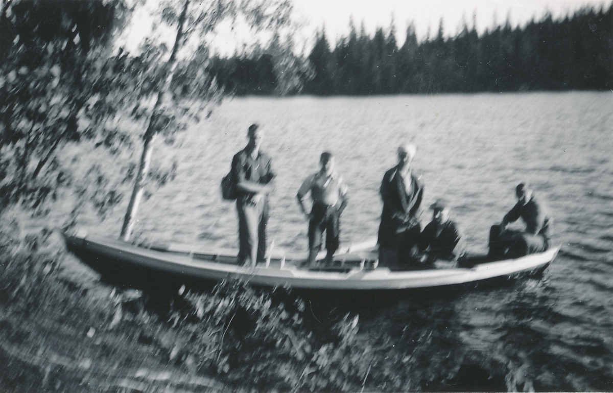 Fem personer i en trebåt, en pram, på innsjø.