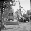 Kranbil och lastbil utanför stationshuset i Mariefred. Mitt i bild ses Museijärnvägen, Östra Södermanlands Järnväg, ÖSlJ ackumulatorlok 15.