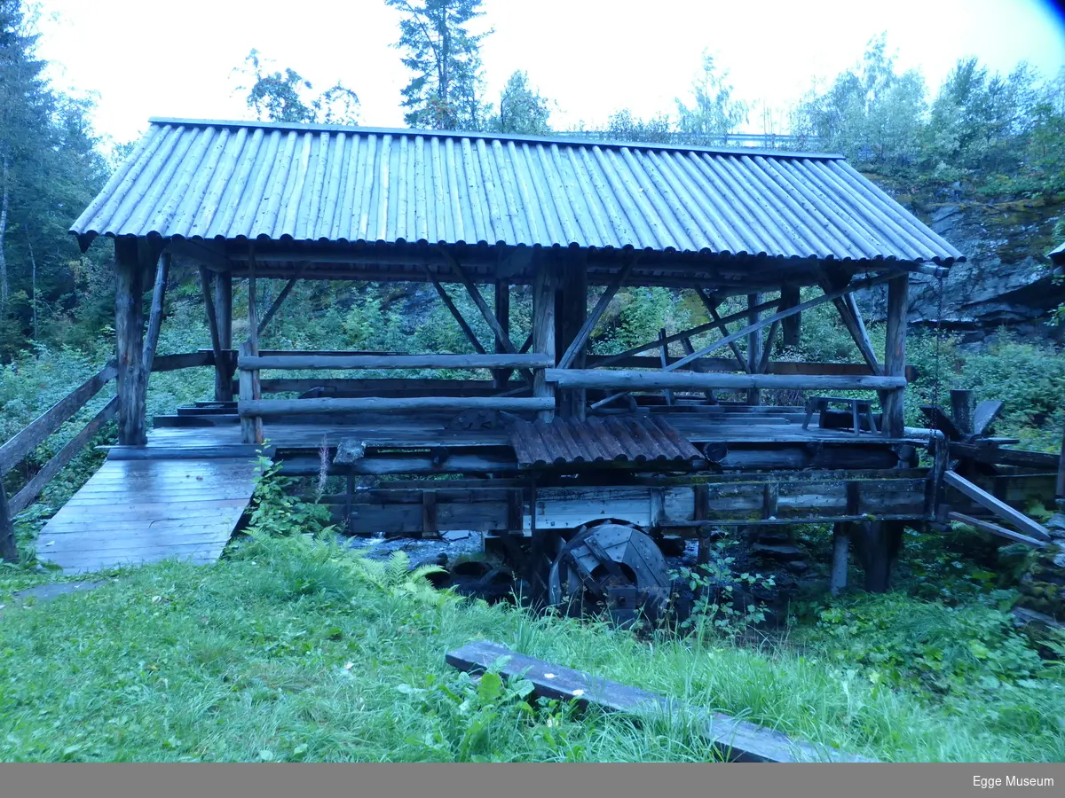 Oppgangssag i reisverk. Stående stolper på svilla i hvert hjørne og midt på hver langside. To skråavstivere på hver av de 6 stolpene som bærer raftestokken. Trerampe med rekkverk.