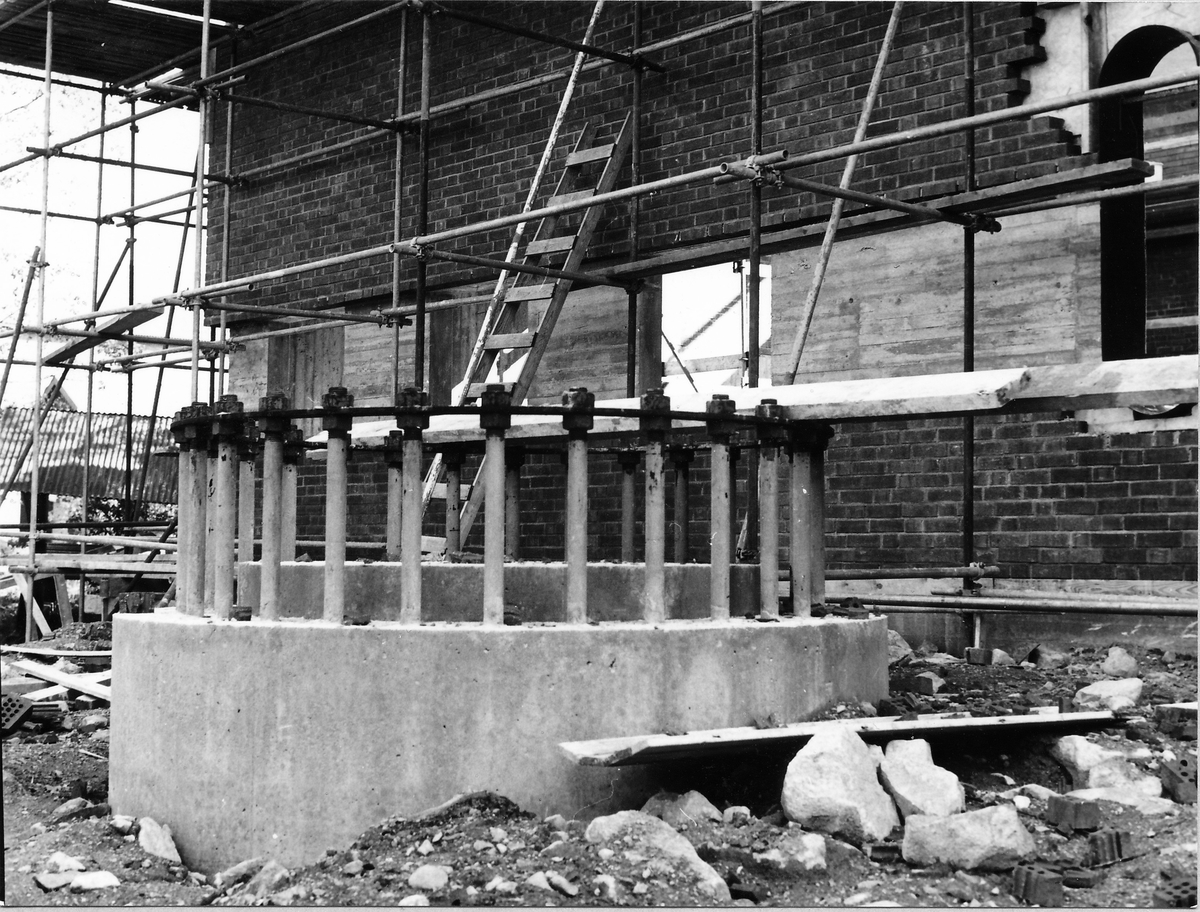 Montering av skorsten på regementets nya värmecentral den 10 oktober 1972.
Obs. Tio bilder.
Bild 1: Fundamentet på vilken den stora skorstenen skall skruvas fast.
Bild 2: Övre halvan av skorstenen under förflyttning till sin monteringsplats.
Bild 3: Nedre halvan av skorstenen håller på att lastas av från lastbilen. I bakgrunden syns den nya byggnaden till maskincentralen.
Bild 4: Nedre halvan läggs ned på stöd.
Bild 5: Den övre halvan av skorstenen, på yttersidan syns påsvetsade plåtspiraler för vindstabiliseringen.
Bild 6: Det krävdes kraftiga kranar för att klara alla lyft. I bakgrunden syns by 10 (Sörmlandssalen, markan och ubefmäss)
Bild 7: Flera kranar i samverkan för att få den nedre skorstenen i rätt läge.
Bild 8: Nu är skorstenen hopsatt och lyftet påbörjat.
Bild 9: Lyftet fortsätter, i förgrunden dom två oljecisternerna.
Bild 10: Nu står skorstenen på plats.