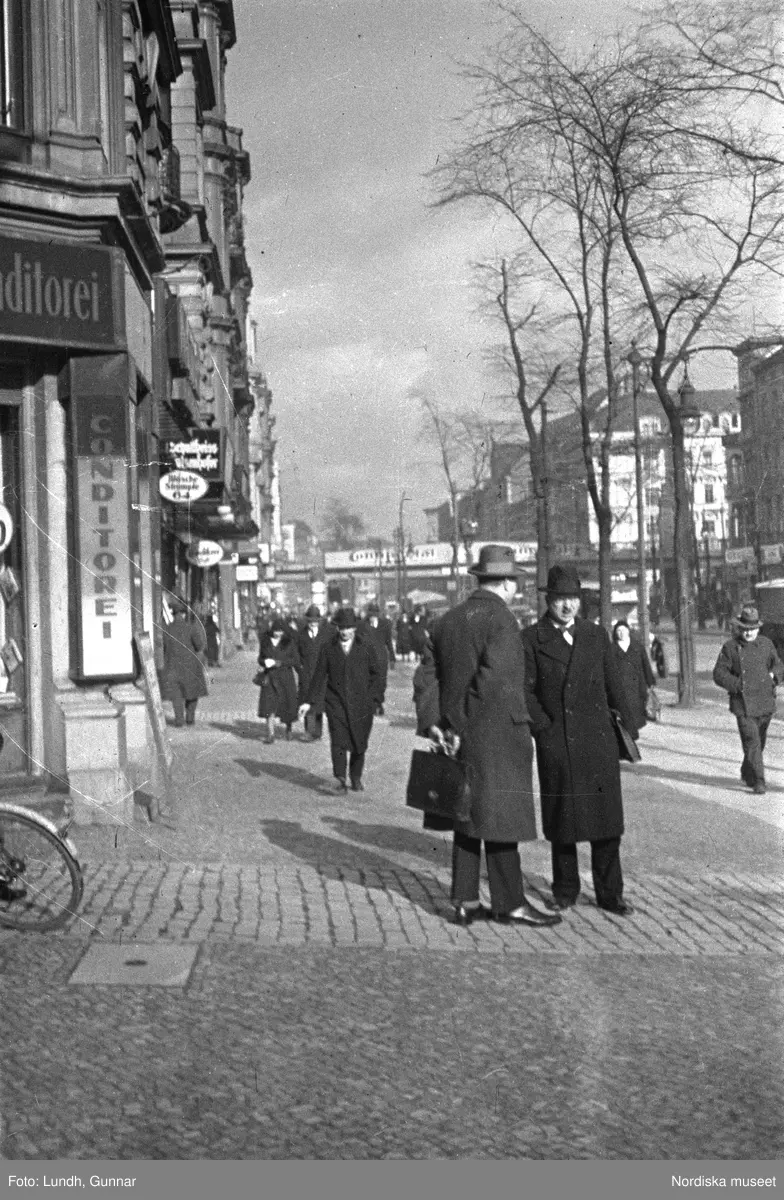Motiv: Tyskland, Berlin;
Porträtt av en man "Tiller" som dricker ur ett glas.

Motiv: Tyskland, Berlin;
Utsikt från ett restaurangfönster över ett torg med torghandel, en man står vid ett försäljningsstånd med skylt "Sie husten nicht mehr!.....", gatuvy med en cyklist och en bil, gatuvy med bilar och en man som skjuter en kärra med text "G. Pabst Lack-Fabrik", skylt "Diese Villen sind im ganzen oder geteilt zu vermieten.....", grind med skyltar "Prof. Georg Klempener" "Professor Dr. A. Pinkuss", gatuvy med an man som samtalar med en kvinna, ett bord på gatan med böcker till försäljning, skylt "5 zimmer wohnung 1 etage auch geteilt per 1. april näheres b. wirt.", exteriör av byggnad med stor skylt på fasaden "Zu vermieten....", gatuvy med bilar - spårvagn - man med handkärra och en man som sopar gatan.