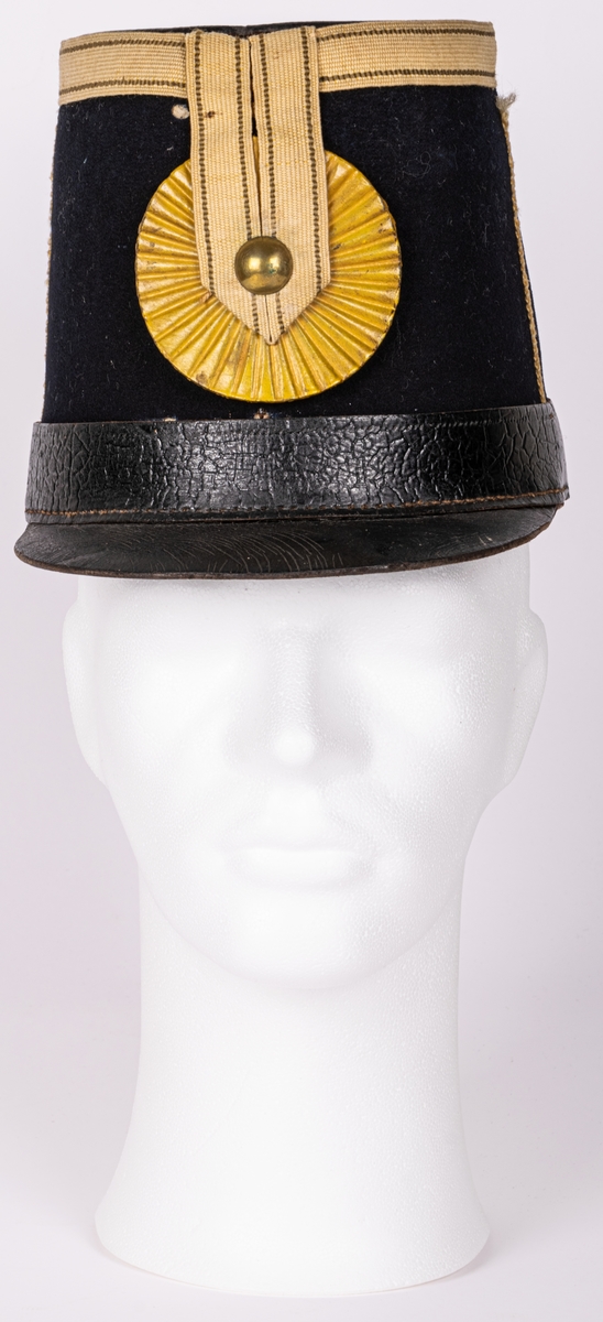 Militärhatt, "kepi". Från Hälsinge regemente 1856 (58?)-1865. 
Kepin är av mörkblått tyg, klädd med läder ovanpå, gulvit tygremsa runtomkring ovankanten samt dubbelt rakt ner framtill jämte gul skiva (trä), med radiära räfflor samt mässingsknapp ovanpå. M/1854.