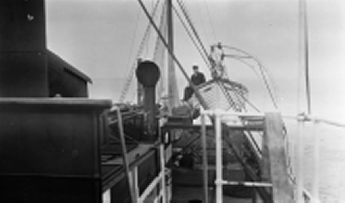 Ombord på D/S STORFOND sett mot akter. En mann sitter i livbåt som henger i daviter. Lastet med koks.